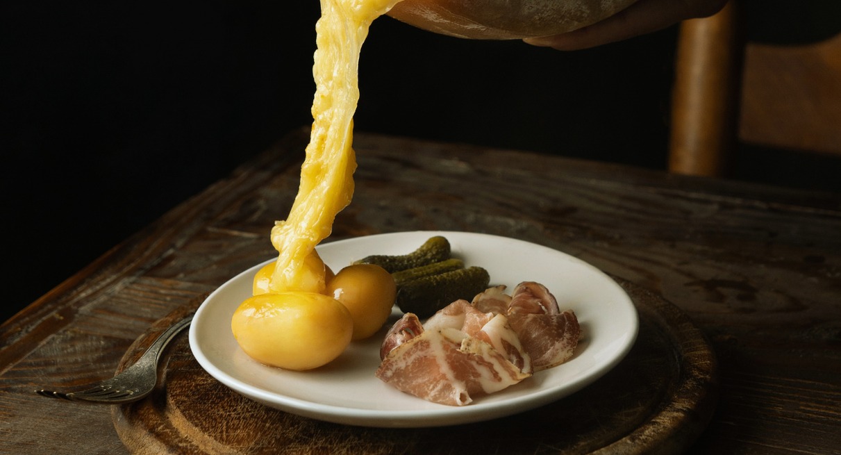 fromage à raclette fondu coulant sur des pommes de terre, cornichons et charcuterie