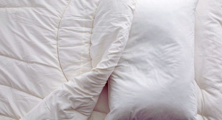 Oreiller blanc posé sur une couette blanche froissée, vu du dessus