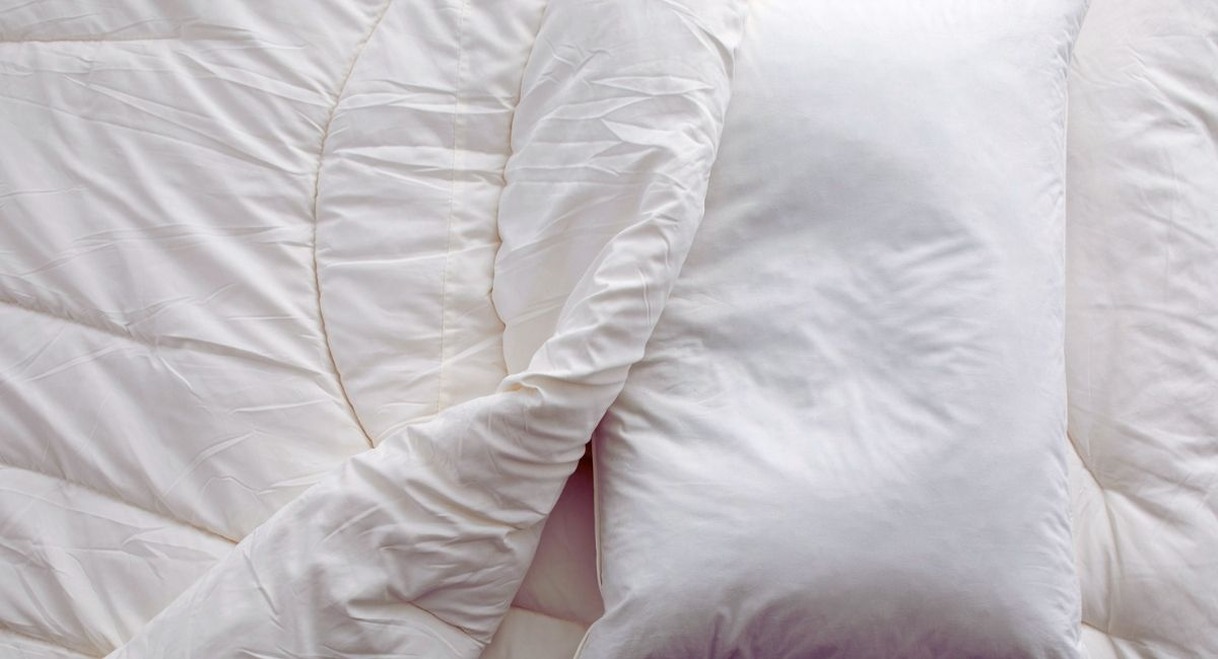Oreiller blanc posé sur une couette blanche froissée, vu du dessus